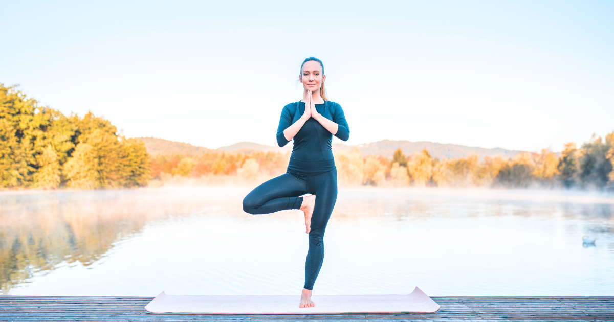 a girl standing on one leg doing tree pose outdoors