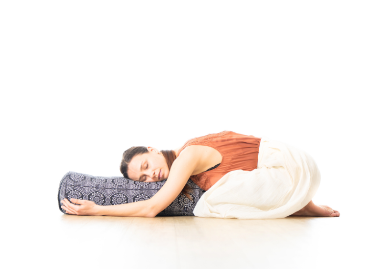 a girl resting in child's pose on a bolster