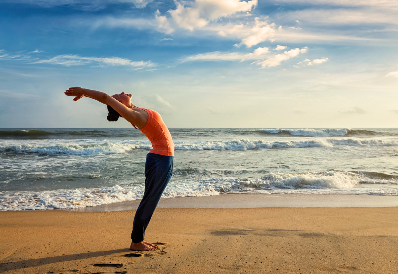 a woman doing standing backbend at the beach