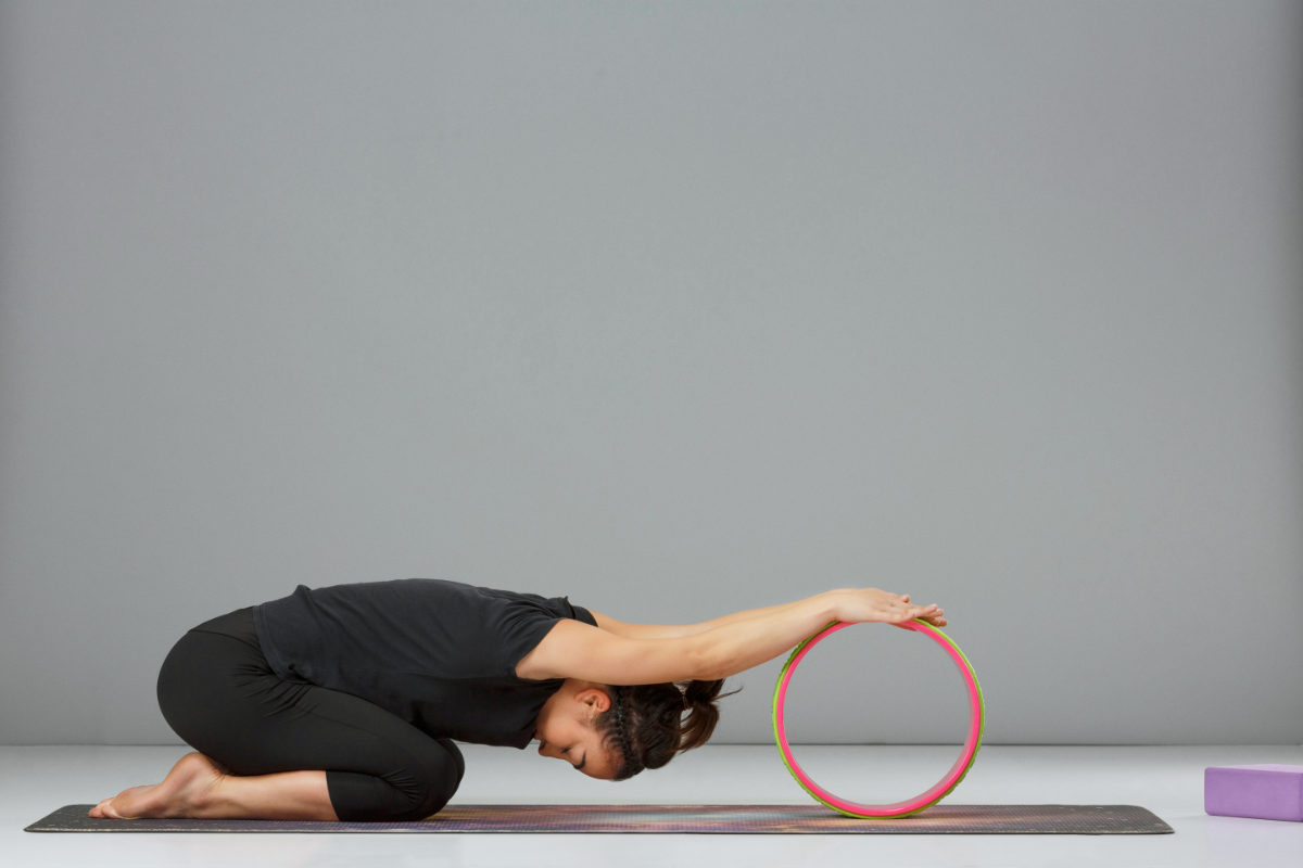 a girl stretching using a yoga wheel in child's pose