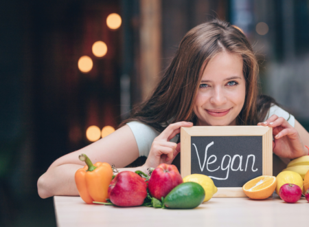 a girl holding a mini black board with vegan written on it and vegetables put on a counter in front of her
